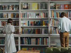 Man in White Dress Shirt Standing Beside Brown Wooden Book Shelf